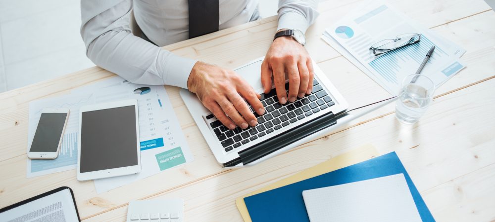 Professional businessman working at office desk and typing on a laptop, unrecognizable person